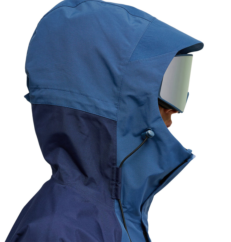 A person in profile wears the DC Shoes Mountain Lab Anorak 10K—a blue hooded jacket paired with ski goggles—set against a white background. The jacket offers breathable protection for comfort and optimal snow performance.