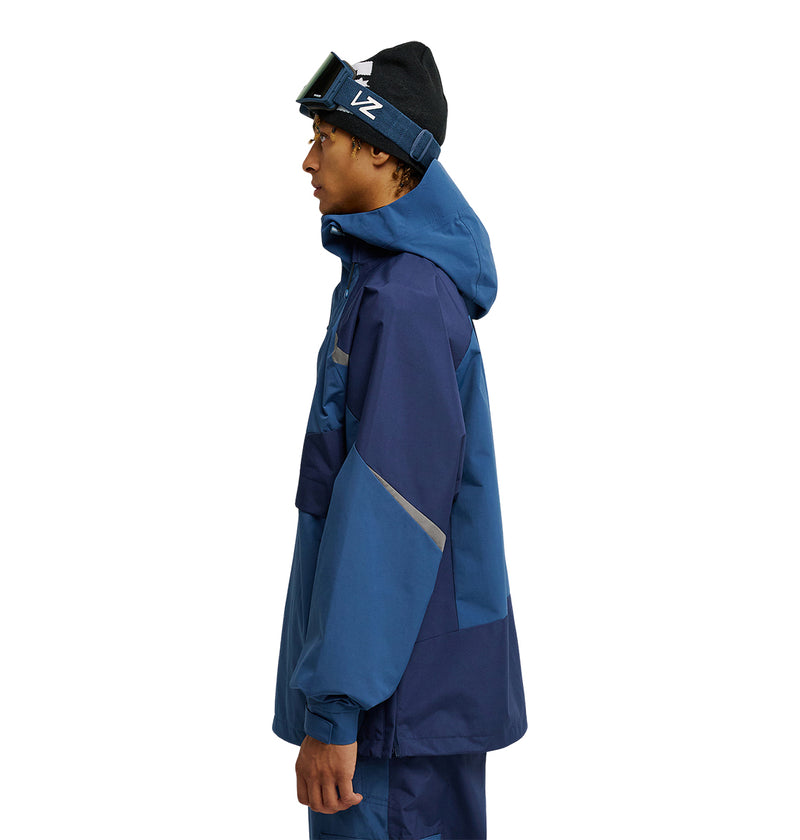 Wearing the DC Shoes Mountain Lab Anorak 10K—a blue hooded jacket paired with matching blue pants and a black beanie topped with ski goggles—for optimal snow performance and breathable protection, a person stands in profile facing left against a white background.