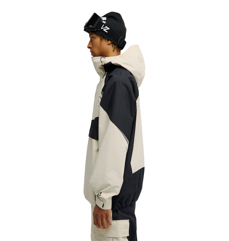 A person in profile wearing the DC Shoes Mountain Lab Anorak 10K—a black and beige hooded snow jacket with breathable protection—along with matching pants, a black beanie, and ski goggles resting on their forehead, stands against a plain white background.