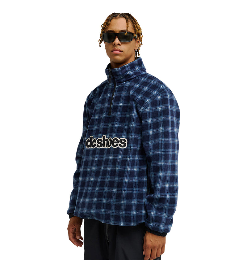 A person wearing sunglasses and the DC Shoes Park Reversible Anorak in blue plaid, featuring “dcshoes” printed on the front, standing against a white background.