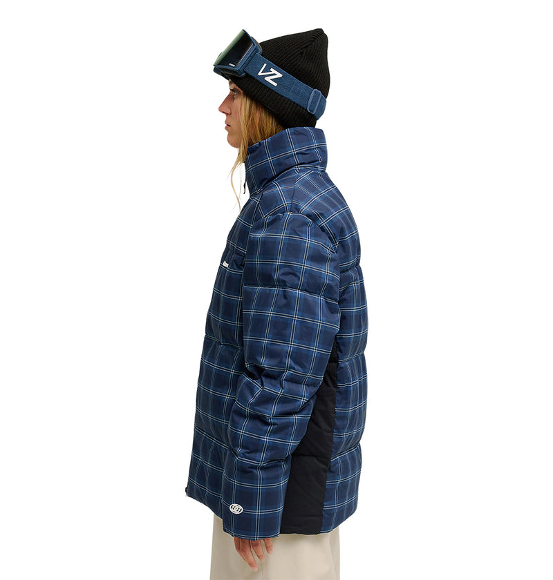A person in profile wears a black beanie, ski goggles, and the DC Shoes Trackstar Puffer 10K blue plaid insulated winter jacket with beige pants, standing against a white background.
