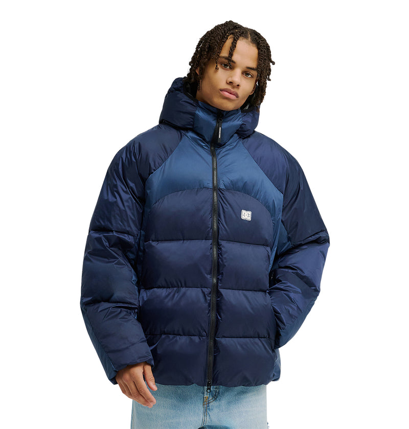 A person wearing the DC Shoes Powder Puffer 10K jacket in navy blue, featuring a hood, front zipper, and a small DC logo on the chest, along with light blue jeans stands against a plain white background. The jacket is designed with high-quality insulation to provide reliable warmth in colder conditions.