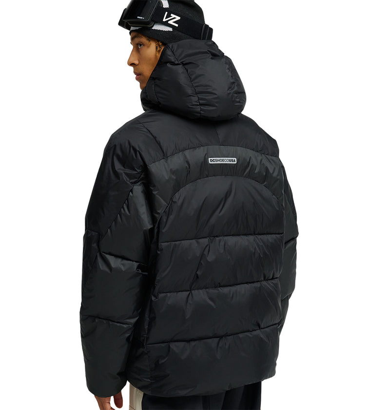 A person wearing the DC Shoes Powder Puffer 10K—a black hooded jacket designed for top snow performance—stands facing away, glancing over their shoulder. The jacket features a small rectangular logo on the back and delivers breathable, element-resistant protection.