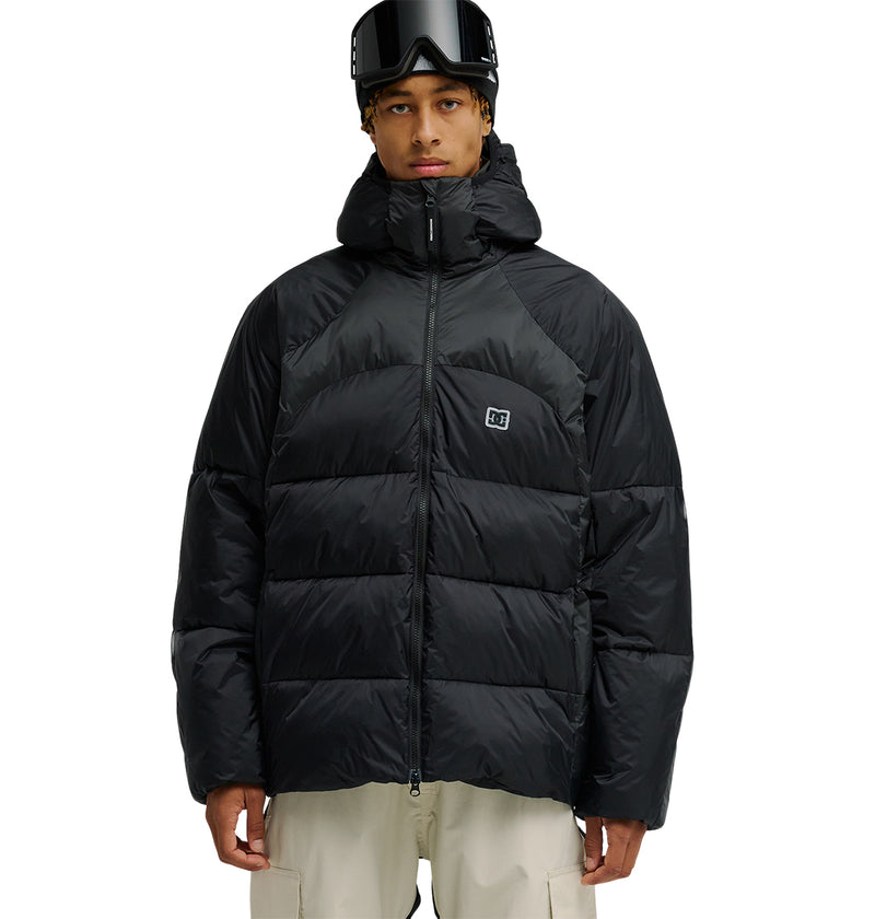 A person wearing the DC Shoes Powder Puffer 10K jacket, paired with off-white pants and ski goggles, stands facing forward against a white background, highlighting snow-ready gear engineered for breathable protection.