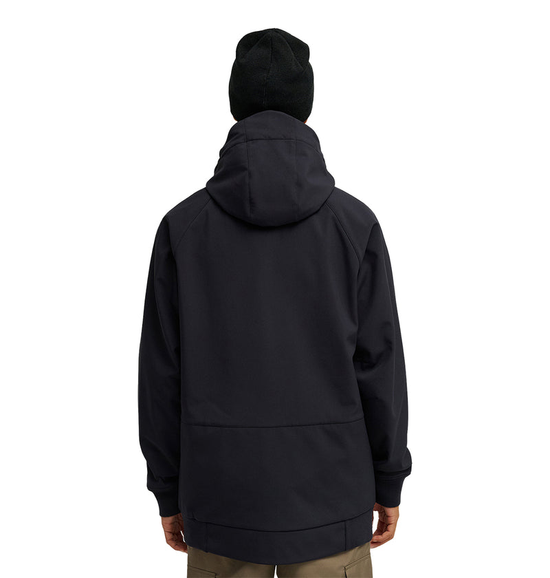 A person is shown from the back wearing a black DC Shoes Spectrum Softshell Jacket with the hood up and a black beanie, paired with khaki pants. The background is plain white.