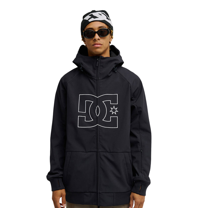 A person wearing the Spectrum Softshell Jacket by DC Shoes—a black softshell jacket featuring a large DC logo—paired with black sunglasses and a black-and-white beanie, stands against a plain white background. The Spectrum Softshell Jacket provides breathable protection for enhanced comfort and style.