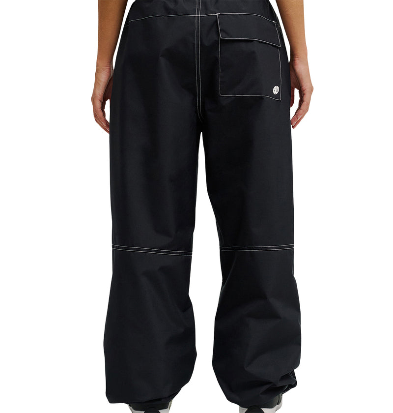 Person shown from the back wearing loose-fitting black DC Shoes Trackstar Pants 10K, featuring contrasting white stitching and a large right back pocket. The hems drape over most of their shoes. Designed for snow performance, these pants offer waterproofing details. Hands rest at their sides.