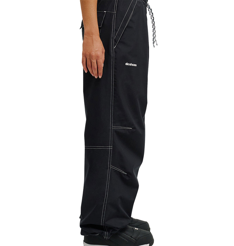 A person is shown from the waist down wearing DC Shoes Trackstar Pants 10K in black, featuring white stitching, black shoes, and a small DC Shoes logo on the upper thigh. The focus is on the breathable protection and stylish design of these waterproof pants.