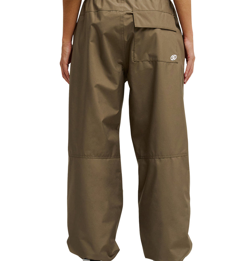 Wearing the DC Shoes Trackstar Pants 10K—loose-fitting, brown waterproof pants with an elastic waistband and pockets—a person stands facing away from the camera against a white background, showcasing breathable protection for all-day comfort.