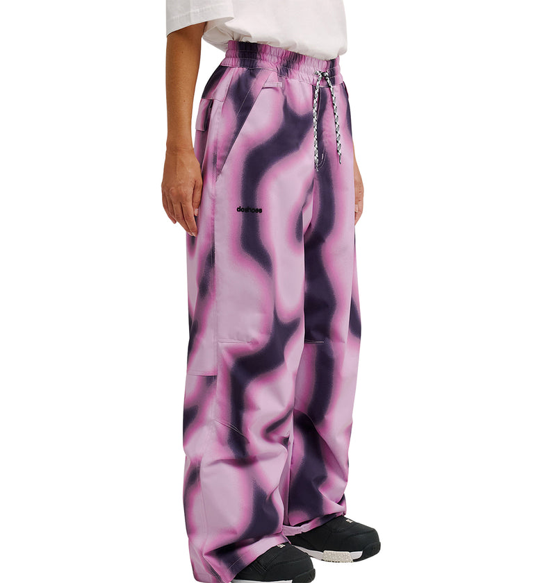 A person wearing DC Shoes Trackstar Pants 10K, featuring a loose fit and pink and black wavy pattern, paired with a white shirt and black sneakers, shown from the shoulders down against a white background.