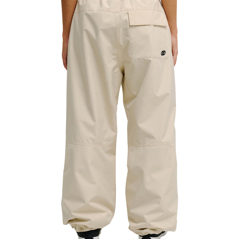 A person wearing loose-fitting, light beige DC Shoes Trackstar Pants 10K with an elastic ankle, seen from the back. Designed for breathable protection, these pants feature a pocket on the right side with a small circular logo above it.