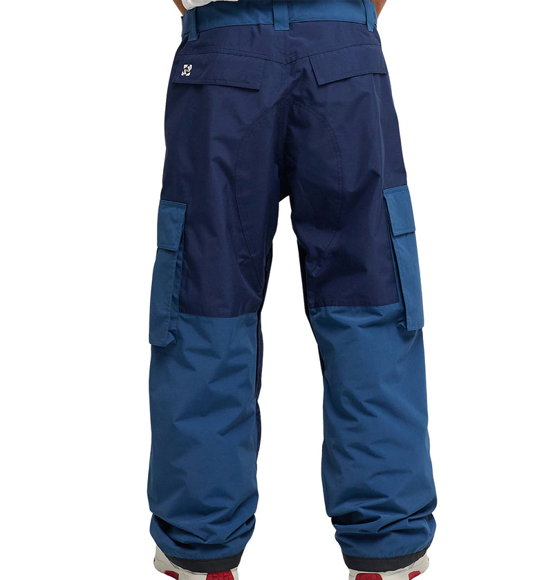 A person stands with their back to the camera, wearing DC Shoes’ Mountain Lab Pants 10K—loose-fitting, two-tone blue cargo pants featuring side and back pockets that offer a stylish blend of breathable protection and modern design.