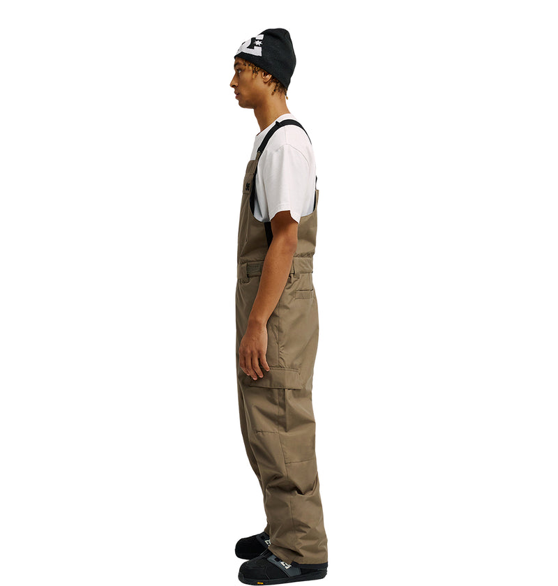 A person wearing a black beanie, white t-shirt, and the Docile Bib 10K by DC Shoes in tan stands in profile against a plain white background, showcasing practical style with breathable protection.