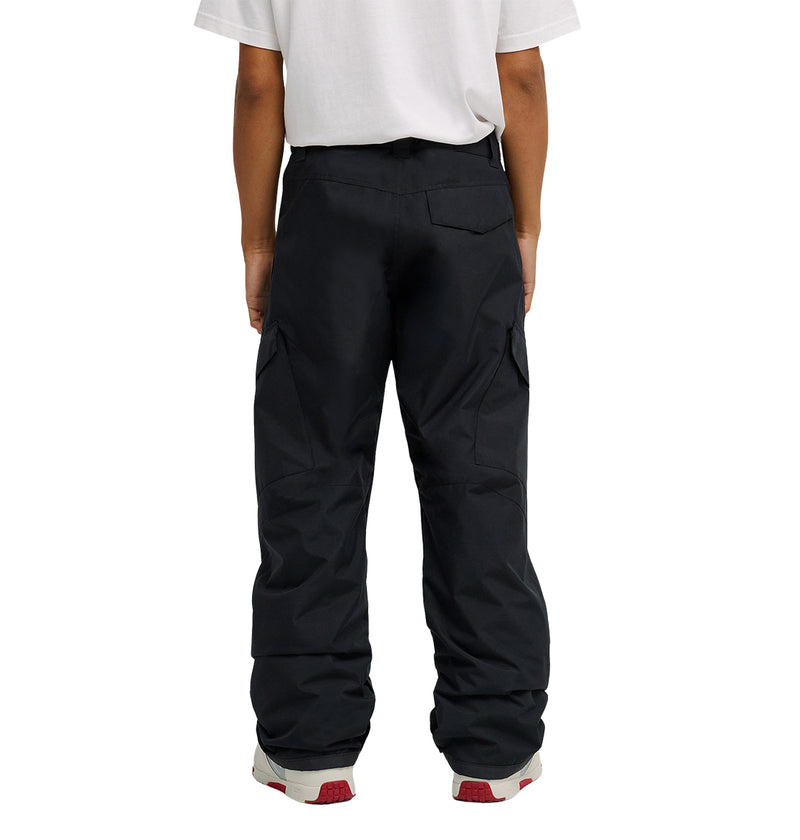 A person is shown from the waist down, wearing a white t-shirt and DC Shoes Banshee Pants—black cargo pants with waterproof insulation—paired with gray and red sneakers. Their back faces the camera.