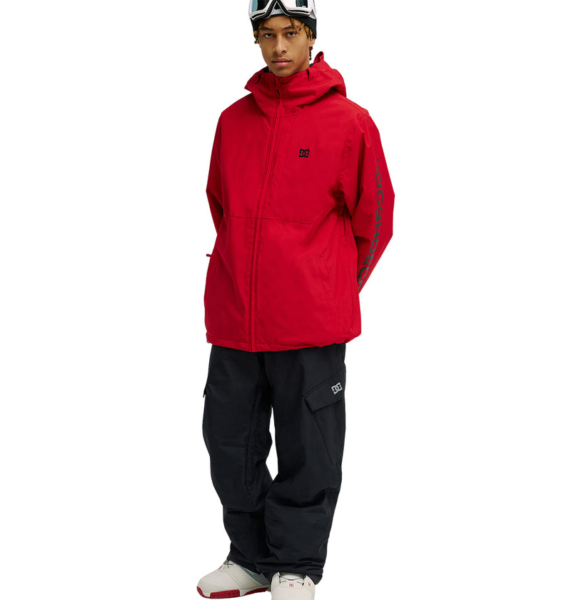 A person wearing black DC Shoes Banshee Pants, a red waterproof hooded jacket, white sneakers with red accents, and ski goggles on their head stands against a white background.