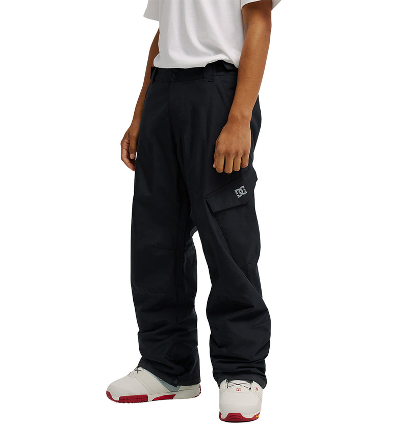 A person wearing a white T-shirt, DC Shoes Banshee Pants—black, waterproof cargo pants with insulation and a logo on the pocket—and white sneakers with red accents, standing against a plain background.