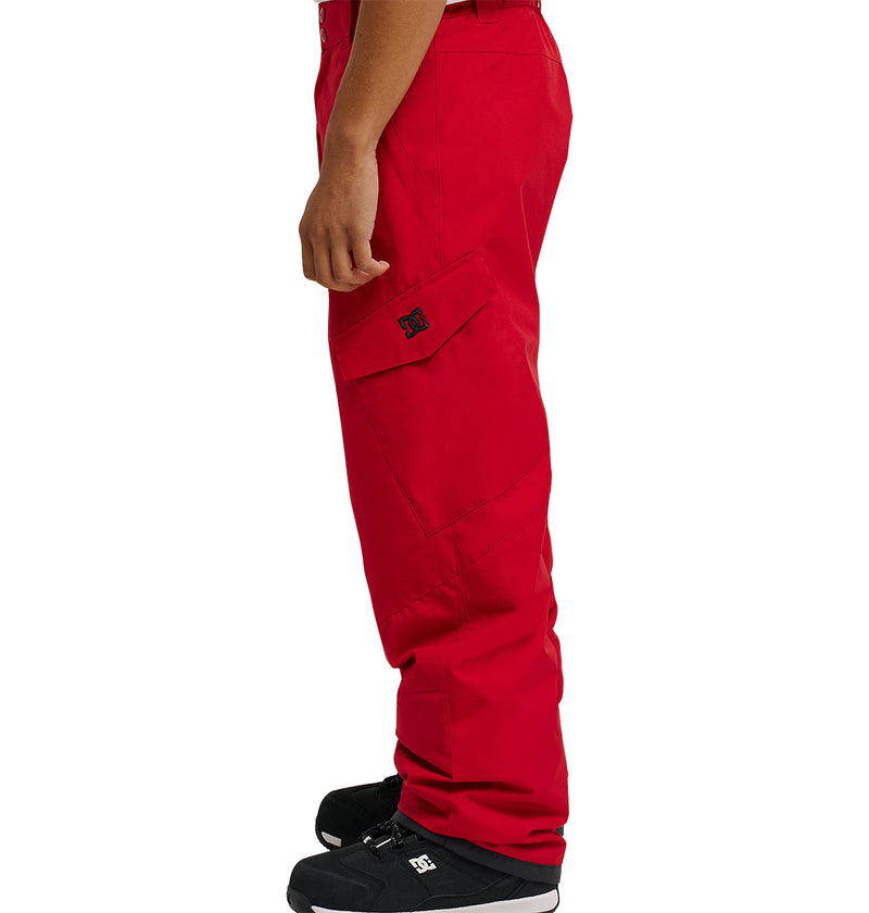A person is standing in profile view wearing DC Shoes Banshee Pants in bright red, paired with black sneakers featuring white soles, against a plain white background.
