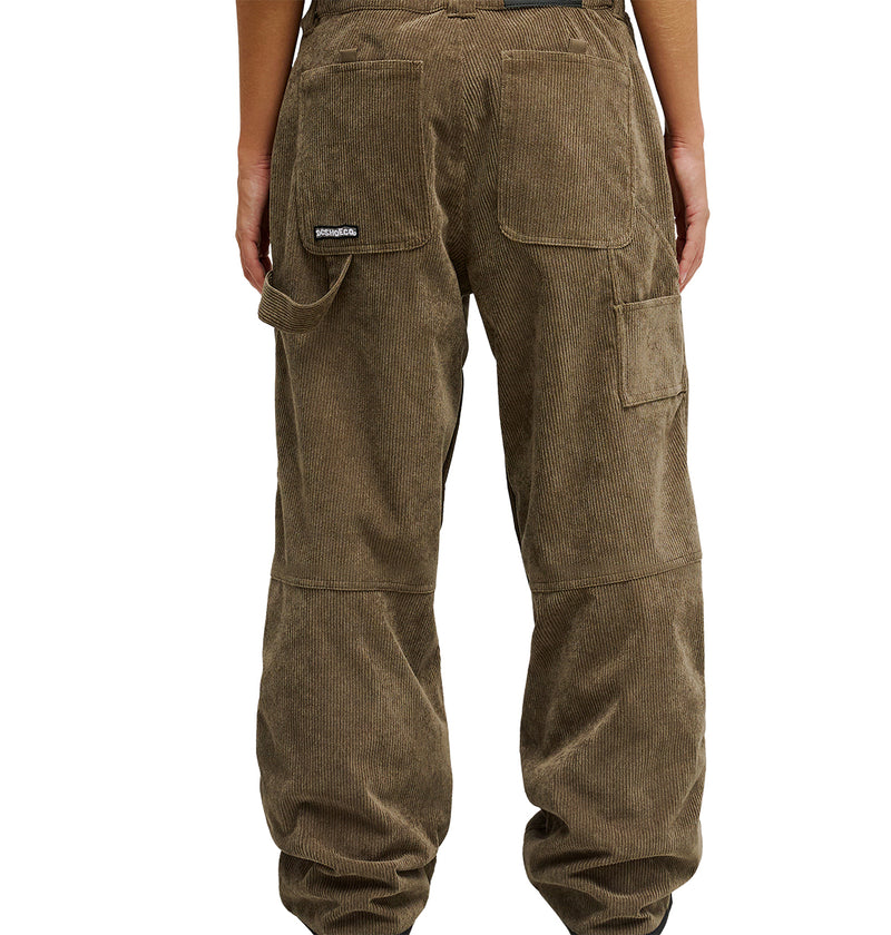 A person is shown from the back wearing the DC Shoes Snow Carpenter Pant 10K in brown corduroy, featuring visible pockets and a small logo patch on the upper left pocket. These pants offer enhanced weather protection and venting for all-day comfort.