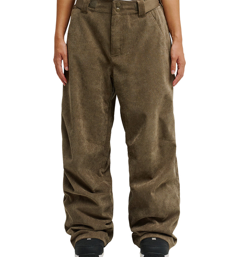 A person is wearing DC Shoes’ Snow Carpenter Pant 10K in loose-fitting brown corduroy, paired with black shoes. Shown from waist to feet against a white background, their hands rest at their sides. The pants feature a textured, ribbed design that delivers comfort and weather protection.