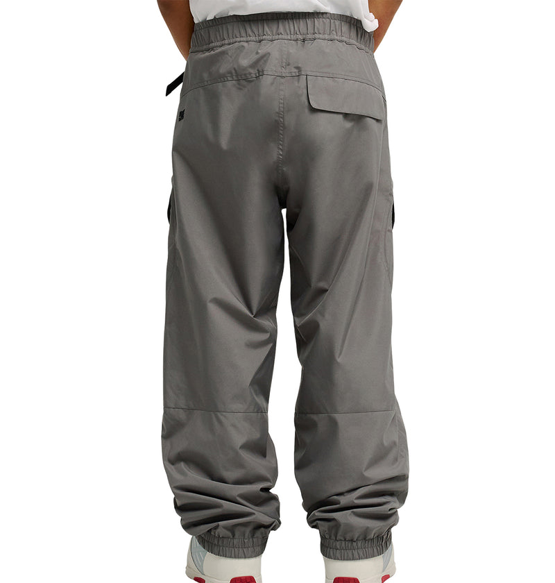 A person is shown from the back wearing DC Shoes Smoke Pants 10K in gray, along with white sneakers, standing with hands in their pockets. These pants feature an elastic waistband and elastic ankle cuffs, providing breathable protection and all-day comfort.