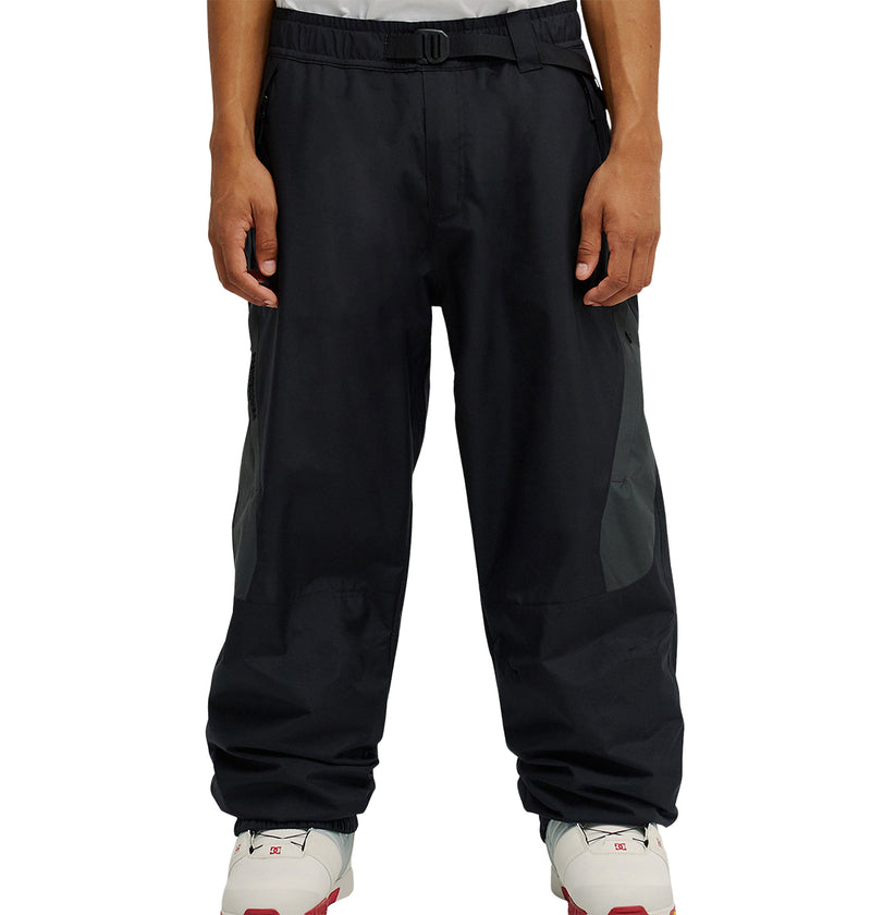 A person wearing DC Shoes Smoke Pants 10K and white athletic shoes stands with arms relaxed by their sides. The photo, cropped at the torso, focuses on the pants and shoes, highlighting the Smoke Pants 10K’s breathable protection for all-day comfort.