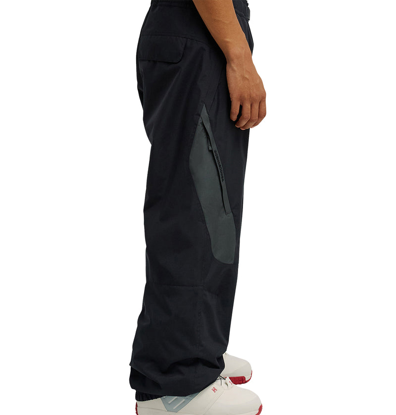 A person wearing DC Shoes Smoke Pants 10K—black pants with a gray zipper pocket—paired with white sneakers, shown from the side against a white background. The Smoke Pants 10K provide breathable protection for all-day comfort.