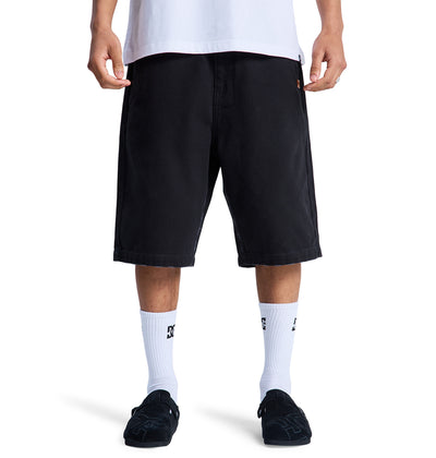 A man is seen from the waist down wearing Reebok Stressed 5 Pocket black knee-length shorts, a white t-shirt, white DC socks, and black slip-on shoes against a white background.