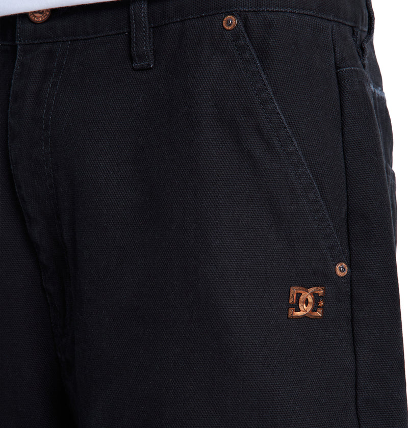 Close-up of black Reebok Stressed 5 Pocket pants showing a small brown logo near the right front pocket, visible seams, and a metal button on the waistband.