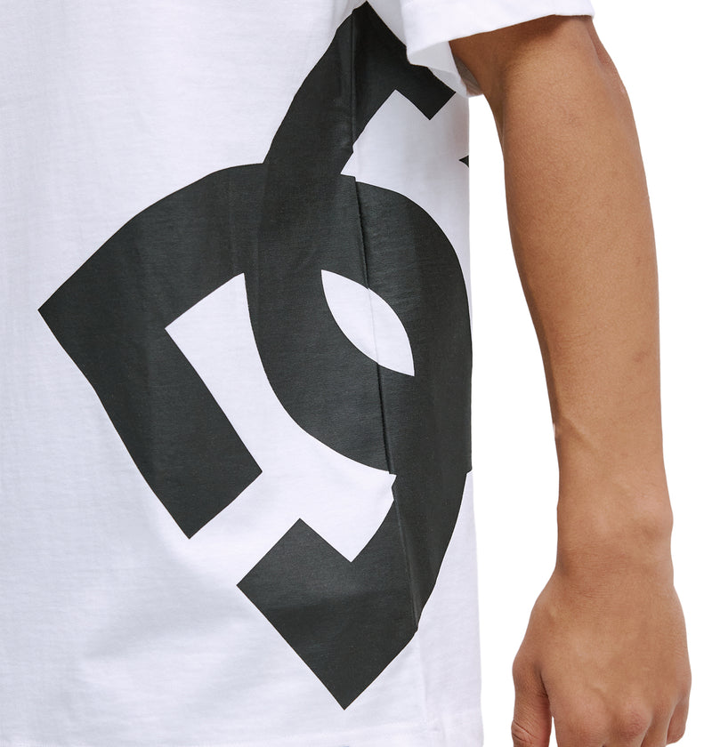 A person wearing a Reebok DC Lanai Hss white T-shirt with a large black graphic and short sleeves, shown from shoulder to arm, with part of the design and their arm visible.