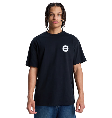 A person with braided hair wears a loose black Reebok Shape Or Destroy Hss t-shirt with a small white logo on the left chest and blue jeans, standing against a white background.