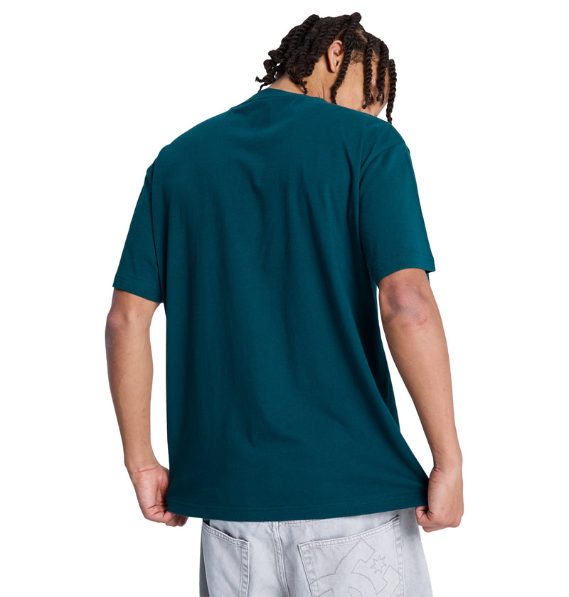 A person with braided hair faces away, wearing a teal Reebok Queltra Lhss short-sleeve t-shirt and light gray shorts, gently pulling the shirt’s hem outward against a plain white background.