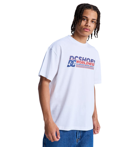 A person with medium-length braids wears a white Reebok Queltra Lhss T-shirt and blue jeans, standing against a plain white background.