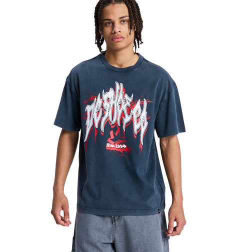 A person with braided hair wears a loose-fitting, dark blue DC Death Machine Hss graphic T-shirt by Reebok with white and red lettering and designs, paired with light blue shorts, standing against a plain white background.
