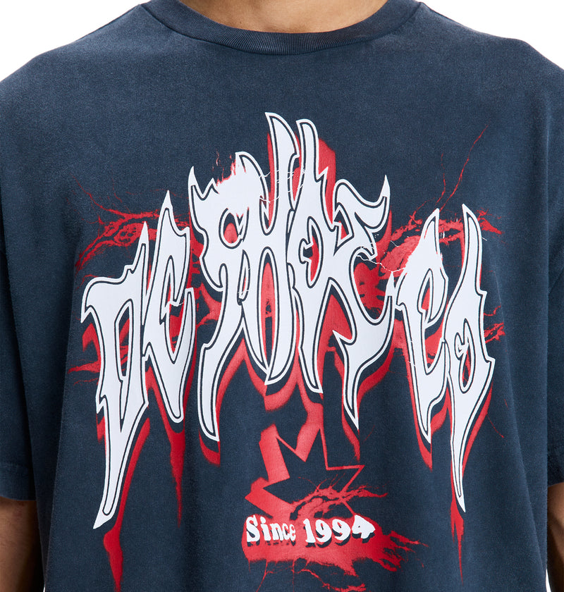 A person wearing a navy blue Reebok DC Death Machine Hss t-shirt featuring bold, graffiti-style white and red DEMARKED text, "Since 1994," and a red graphic design.
