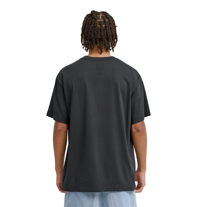 A person with short, twisted hair faces away, wearing a loose black Reebok Strike Twice Hss t-shirt and light blue jeans against a plain white background.