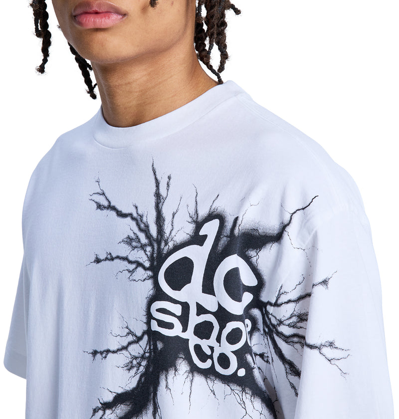 A person wearing a white Strike Twice Hss t-shirt by Reebok, featuring black cracked-line graphic art and bold text on the chest. Their face is partially visible, and they have braided hair.
