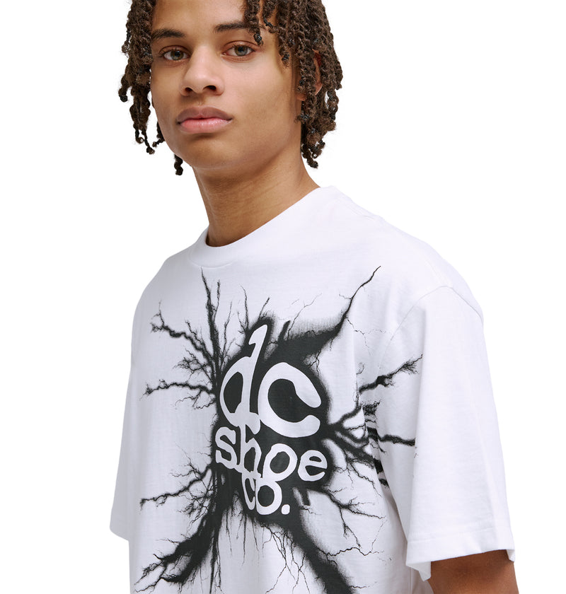Young person with medium-length curly hair wearing a white Reebok Strike Twice Hss T-shirt featuring a bold black graphic design with branching lines around the logo, standing against a plain white background.