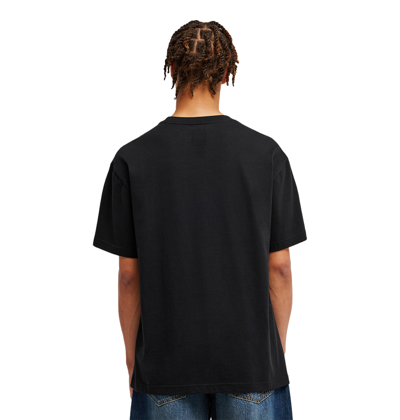 A person with short, twisted hair is shown from behind wearing the DC Shoes Men’s DC Strass Star Tee in black paired with blue jeans, standing against a light gray background.