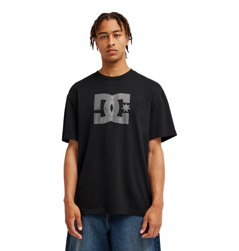 A person stands facing forward against a plain white background, wearing the Men’s DC Strass Star Tee by DC Shoes—a relaxed fit black graphic skate tee featuring a rhinestone DC star—paired with blue jeans.
