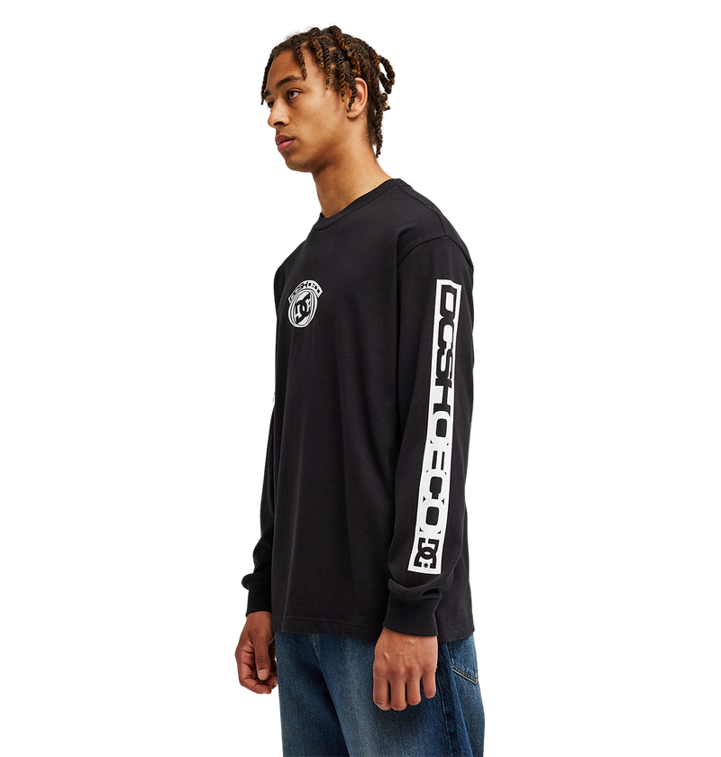 A young man stands sideways against a plain white background, wearing blue jeans and the Men's DC Echo Tee by DC Shoes—a black graphic t-shirt featuring DC artwork on the chest and sleeve.