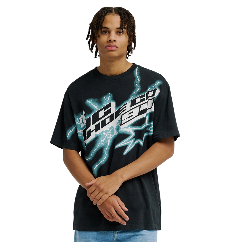A man with short dreadlocks stands against a plain light background with his hands clasped in front, wearing the Men's DC Star Struck Tee by DC Shoes—a relaxed fit black skate shirt featuring bold, abstract white and teal graphics reminiscent of star struck artwork.