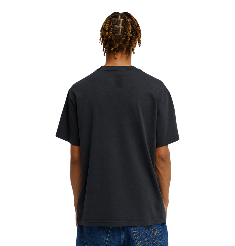 A person with braided hair is seen from behind, wearing the Men's DC Speratic Tee by DC Shoes in black paired with blue jeans against a plain white background.