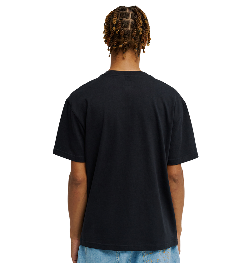 A person with short, twisted braids is shown from the back, wearing the DC Shoes Men's DC Side Flame Tee and light blue jeans against a plain white background, capturing the laid-back style synonymous with skate sessions.