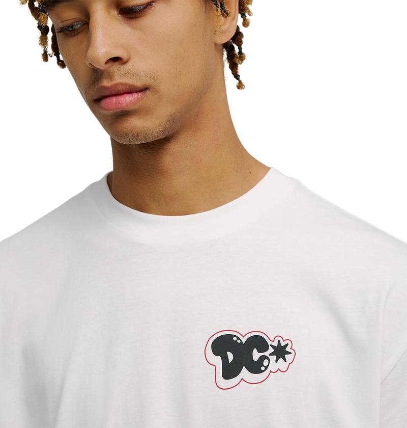 A person wearing the Men's DC Side Flame Tee by DC Shoes, a white graphic skate shirt with a small black and red-outlined DC Shoes logo on the chest. The tee has a relaxed fit, and the person is looking down with a neutral expression.