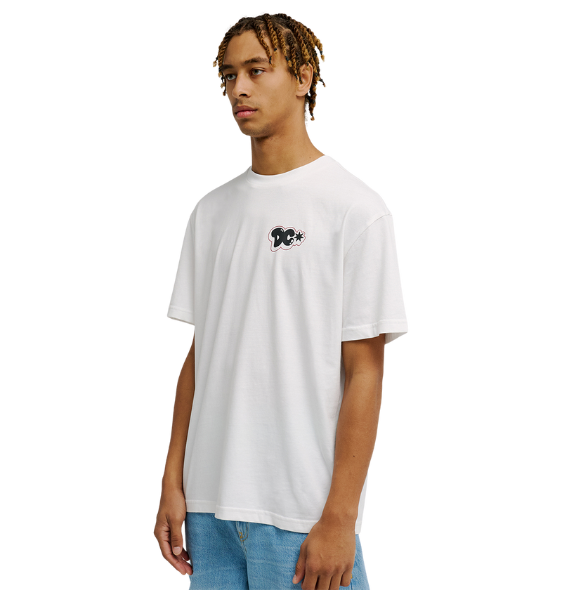A person with short, curly hair wears the Men's DC Side Flame Tee by DC Shoes—a relaxed fit white t-shirt featuring a small black graphic skate tee design on the chest—paired with light blue jeans, standing against a plain white background.