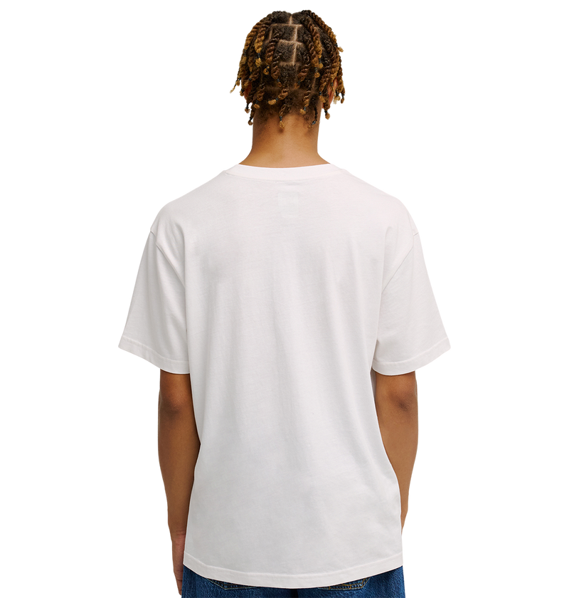 A person with short, twisted hair is seen from behind, wearing a relaxed fit Men's DC Heritage Font Tee by DC Shoes in plain white, paired with blue jeans, standing against a plain white background.