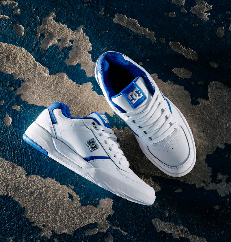 A pair of DC Shoes Men's Fractal S sneakers in white and blue, inspired by pro skater Will Marshall, displayed on a textured blue and gray surface—one shoe facing up and the other on its side—ideal for highlighting street-ready style.