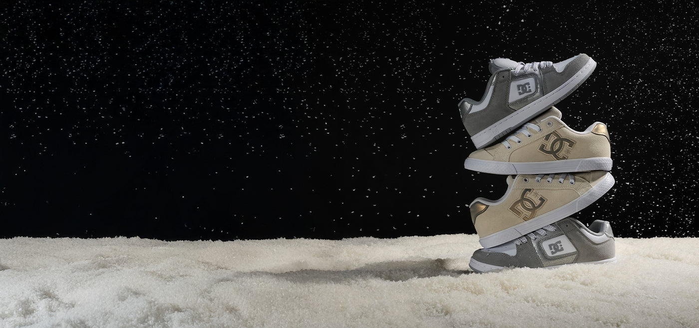 Stack of gray and tan DC sneakers on a snowy landscape with a dark sky.