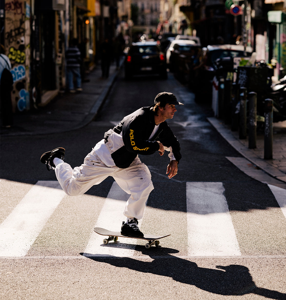 Skateboarder performing a trick on a city street with cars and buildings in the background.