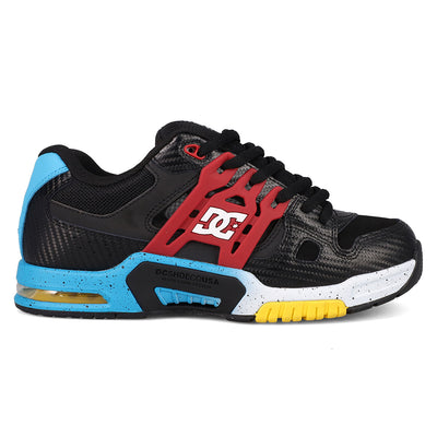 A DC Shoes athletic sneaker in black, red, and blue, featuring a red plastic cage overlay with the DC logo, a black mesh upper, black laces, a white midsole with black speckles, a bright blue heel counter, and a yellow outsole accent.